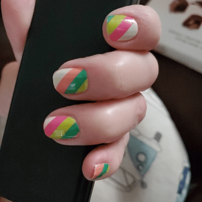 Short nails wearing geometric striped nail wraps in coral pink green diagonal design