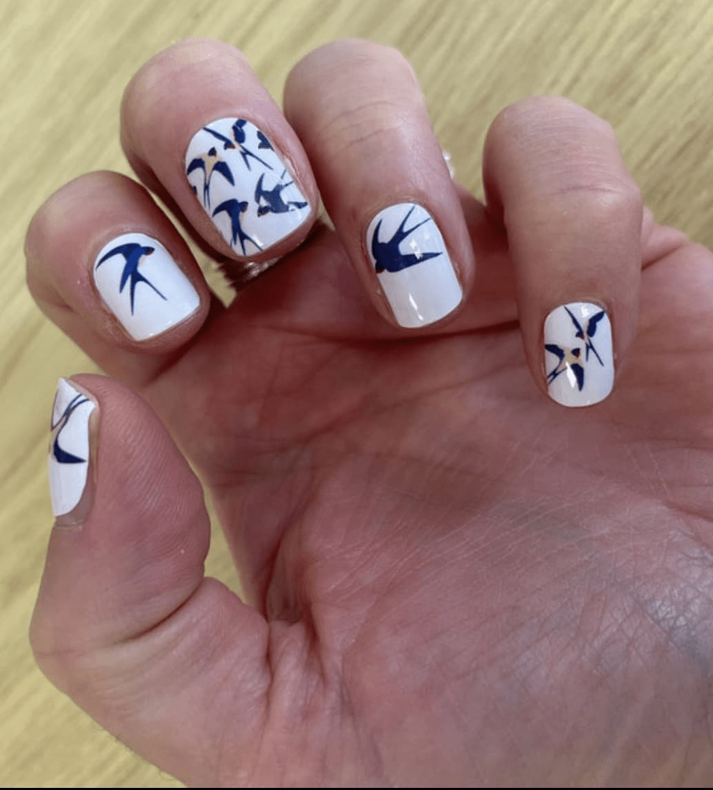 Hand wearing blue swallow nail art wraps on white background manicure