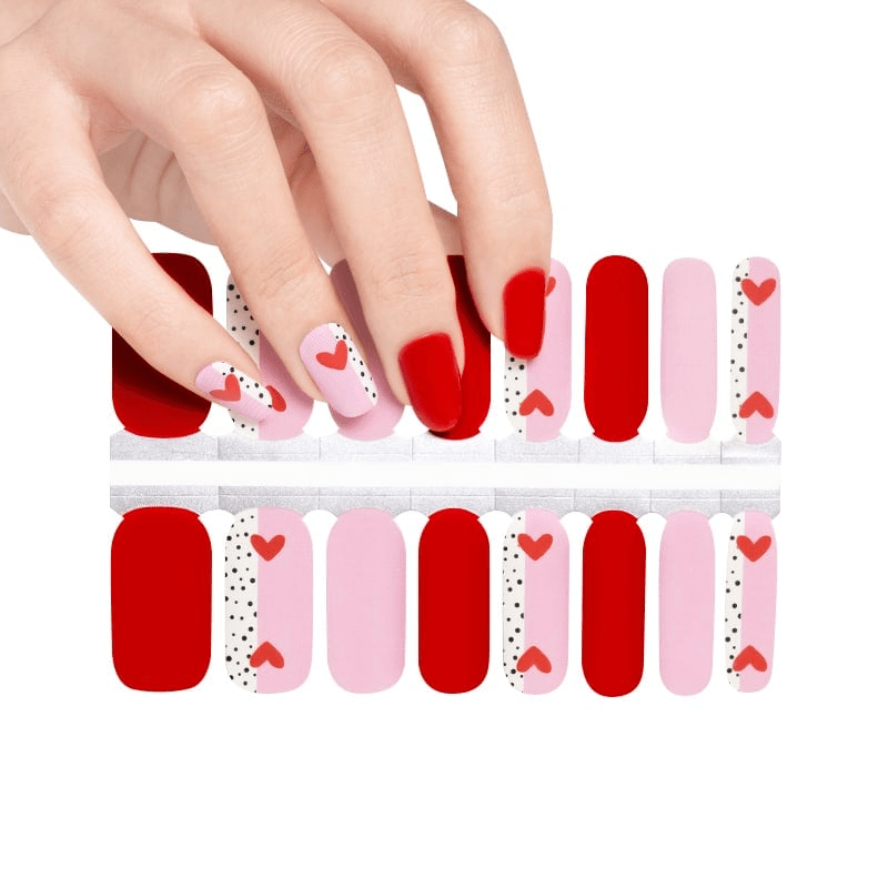 Hand applying red and pink heart nail wraps with polka dot romantic design