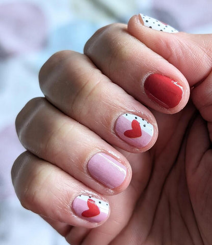 Close-up pink and red Valentine's nail wraps with hearts and dots on fingernails