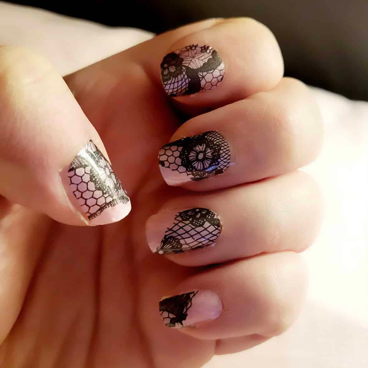 Black lace nail wraps applied on hand showing intricate gothic pattern manicure design