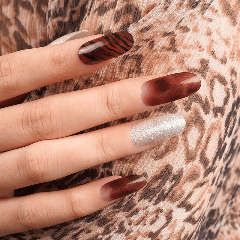 Hand wearing bronze tiger stripe nail wraps with silver glitter accent nails