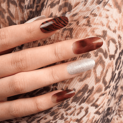 Hand wearing bronze tiger stripe nail wraps with silver glitter accent nails