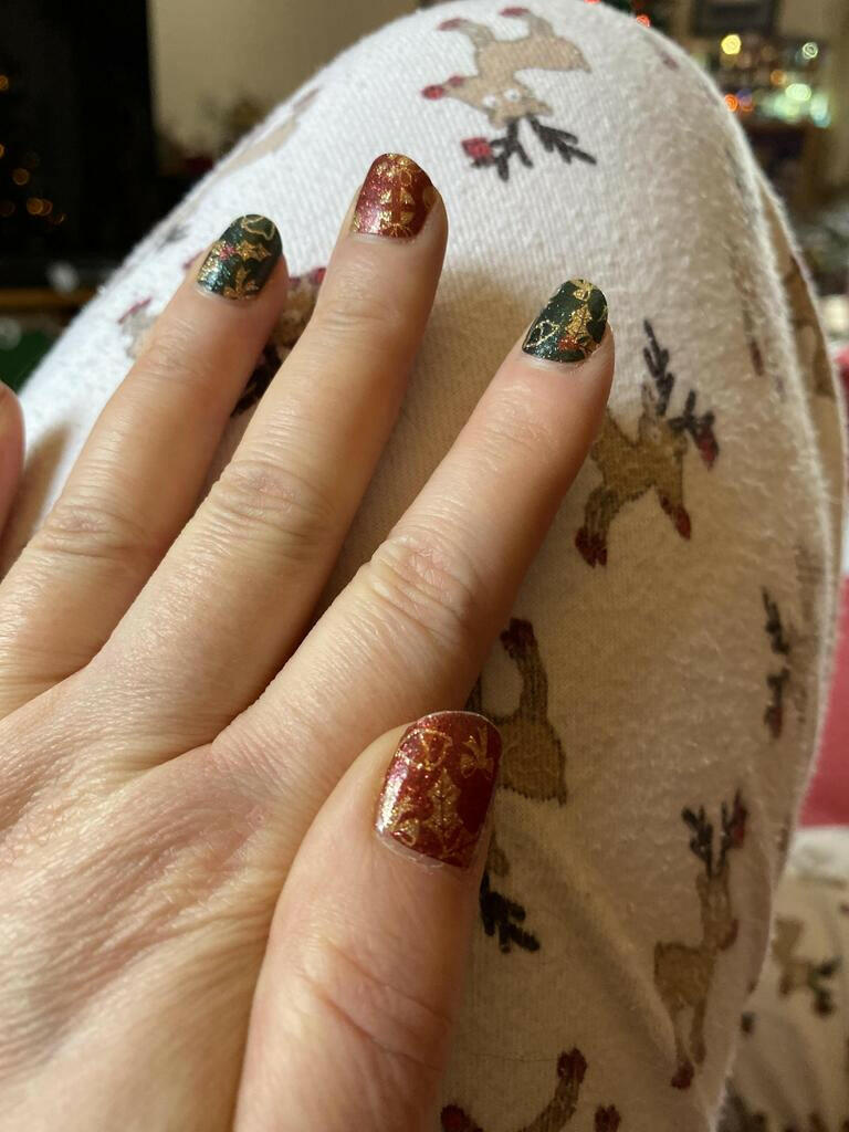 Christmas themed nail wraps on hand with red gold and green festive patterns