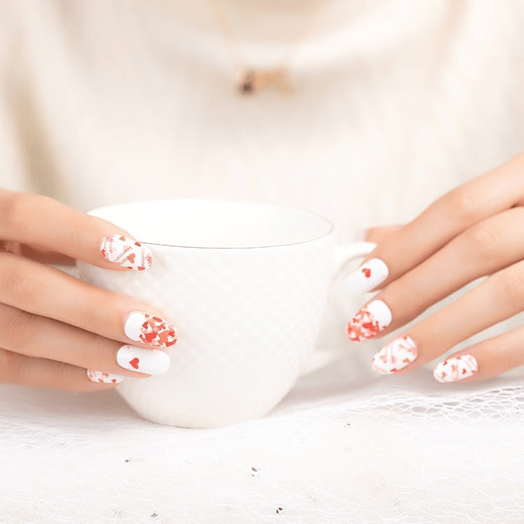 White and red heart pattern nail wraps on hands holding white mug romantic Valentine's design