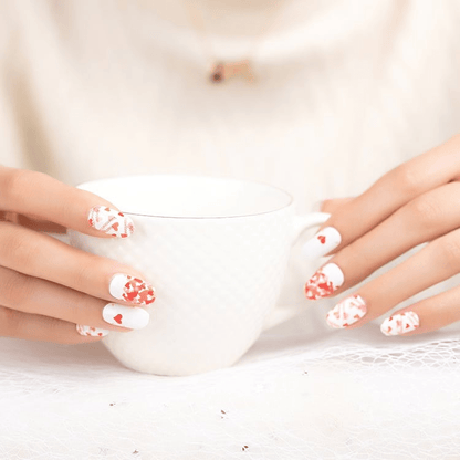 White and red heart pattern nail wraps on hands holding white mug romantic Valentine's design