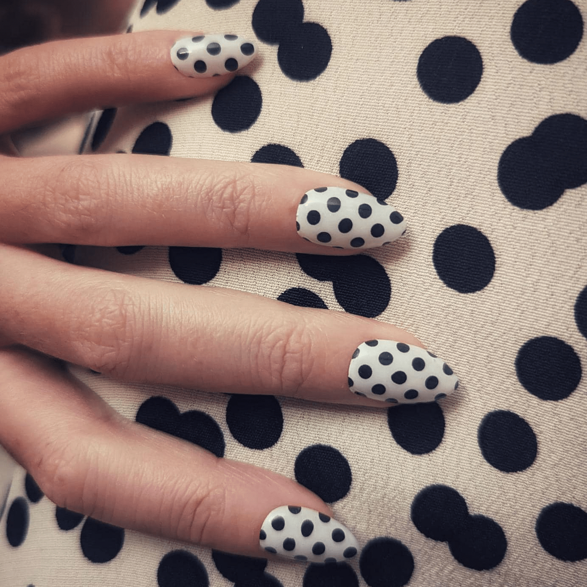 White nail wraps with black polka dot pattern on glossy almond-shaped nails