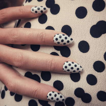 White nail wraps with black polka dot pattern on glossy almond-shaped nails