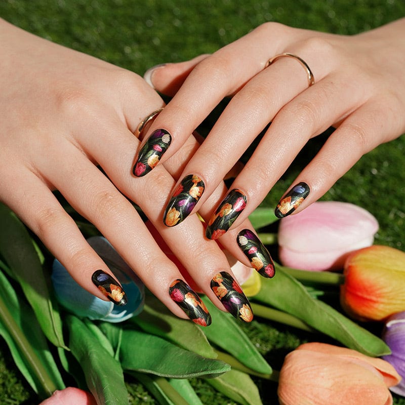 Two hands with dark floral tulip nail art wraps alongside fresh tulip flowers