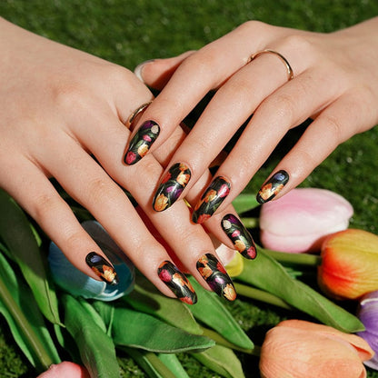 Two hands with dark floral tulip nail art wraps alongside fresh tulip flowers