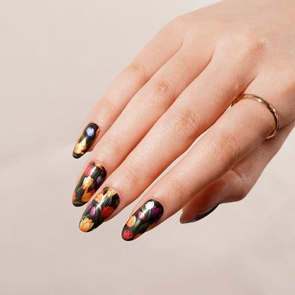 Hand displaying dark floral nail wraps with colourful tulips on black background