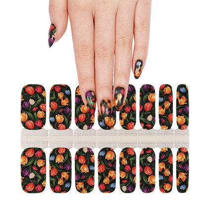 Hand holding sheet of dark floral tulip nail wraps for at-home manicure