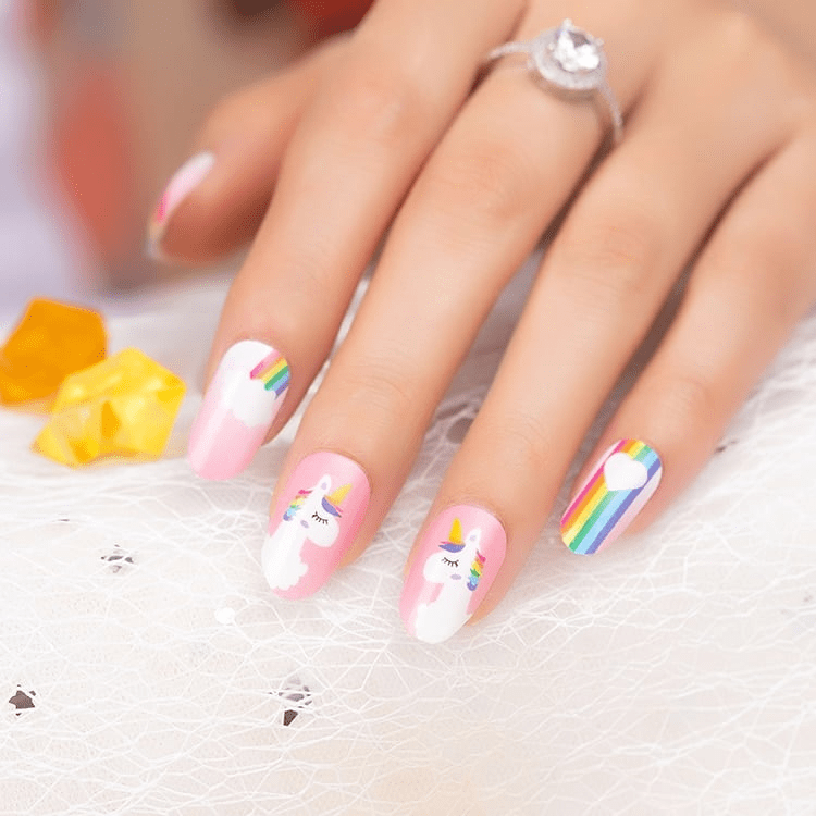 Hand wearing pink unicorn rainbow nail wraps with white clouds cartoon nail art