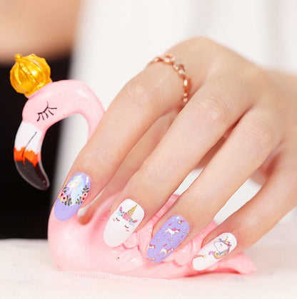 Hand under pink UV lamp curing purple unicorn nail wraps with kawaii cartoon designs