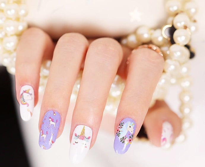 Manicured hand with purple and white unicorn nail wraps featuring cute cartoon designs