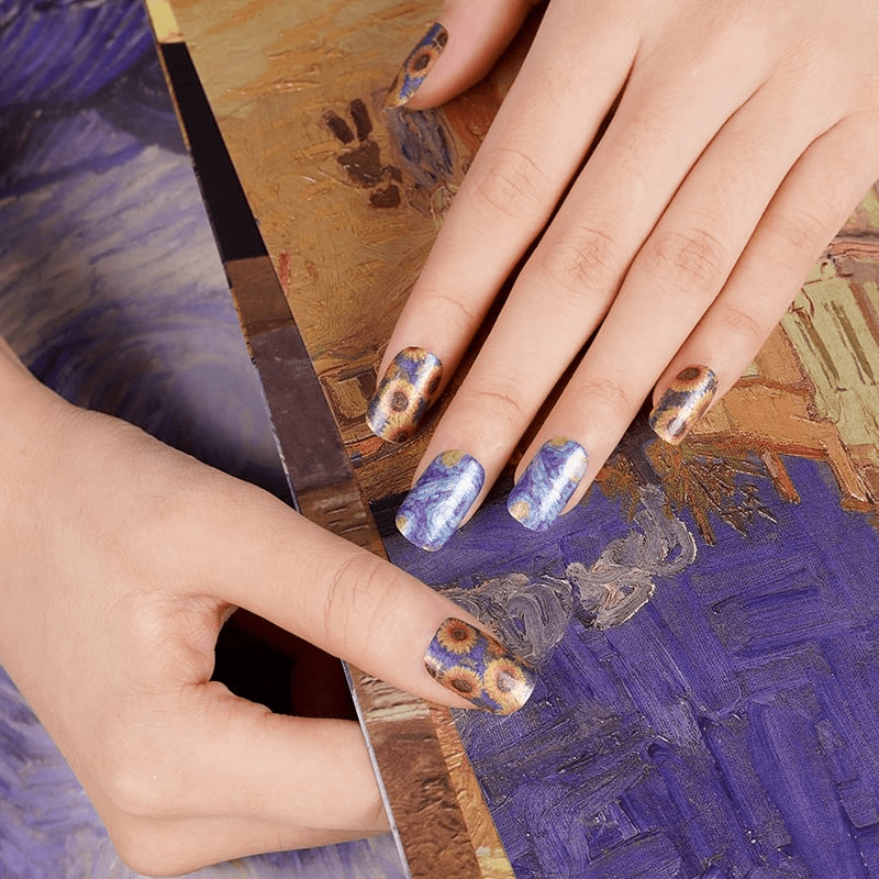 Van Gogh inspired sunflower nail wraps on hands with artistic blue and yellow paint palette