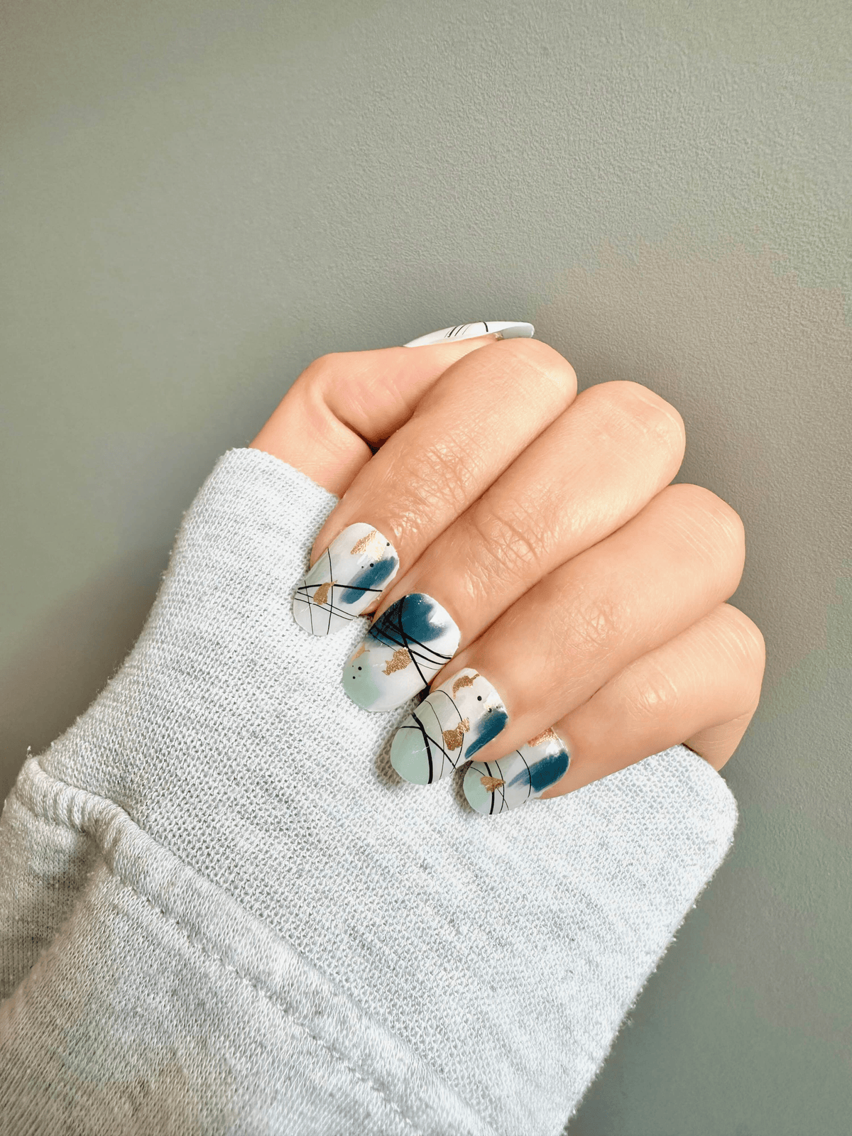 Hand in grey jumper showing contemporary abstract nail wraps in soft blue shades