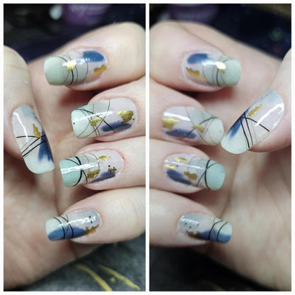 Hand wearing abstract nail art wraps in muted blue and sage green tones