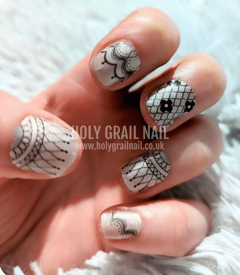 Black lace Victorian nail wraps on hand showing intricate floral patterns on nude base