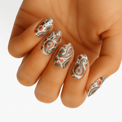 Vintage paisley nail wraps on hand showing ornate orange copper swirl patterns