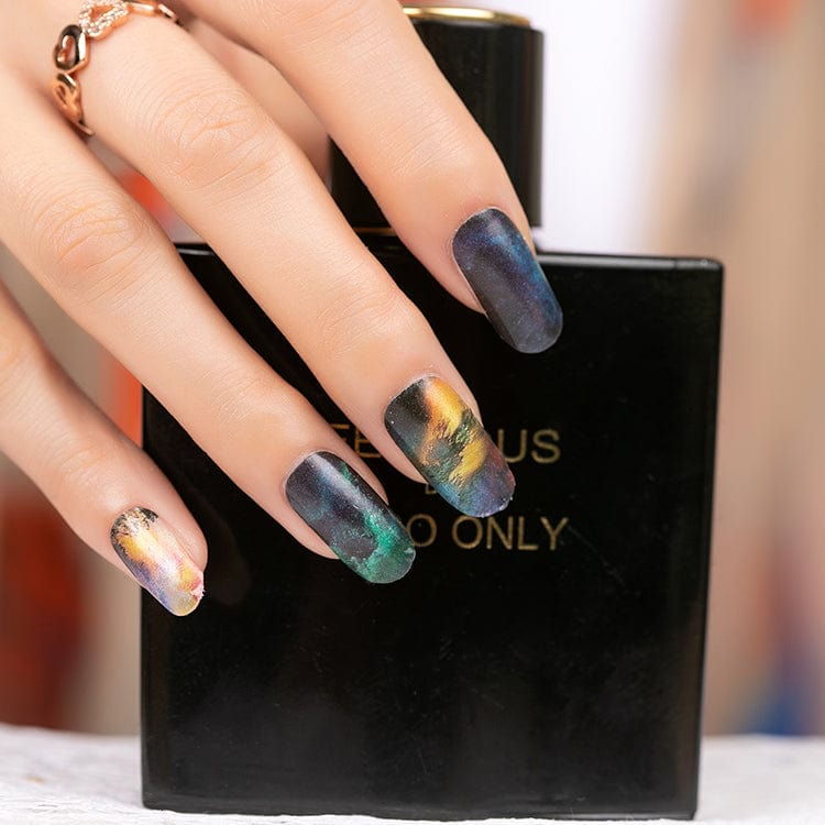 Manicured hand with volcanic marble nail art in emerald green and metallic tones
