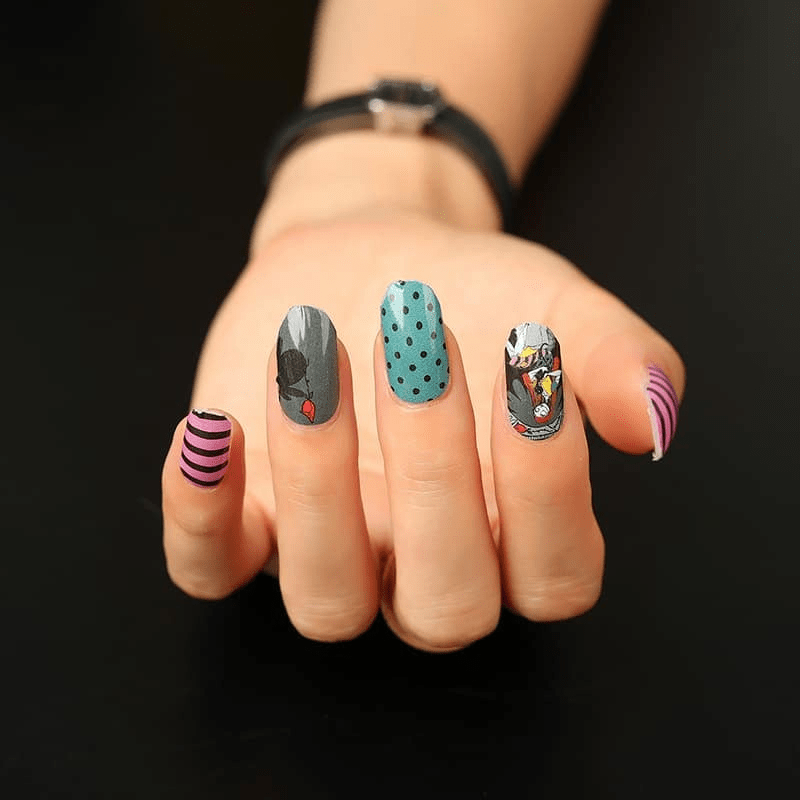 Halloween themed nail wraps on hand featuring black, teal polka dot, pink stripe and character designs