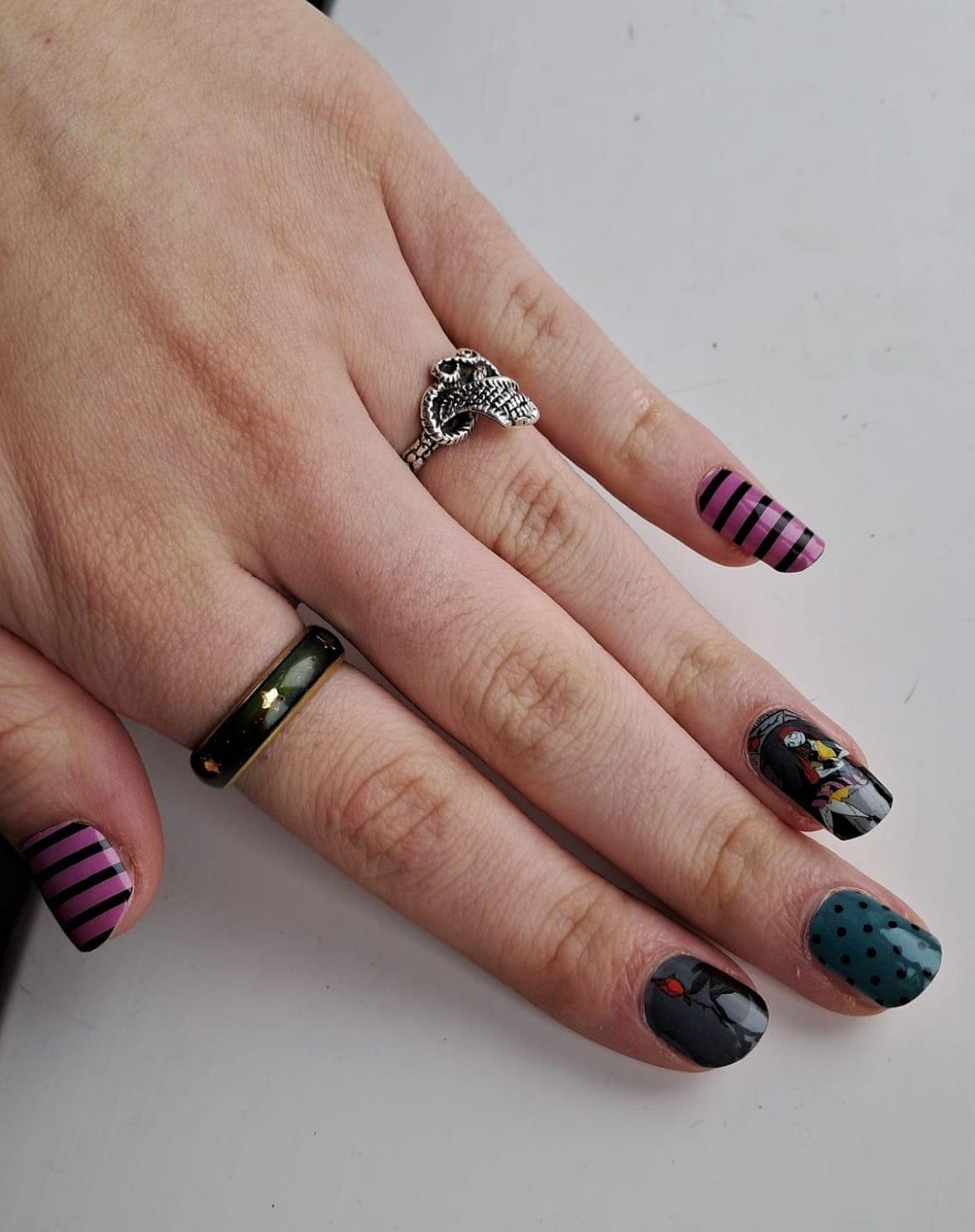 Halloween nail wraps on hand featuring dark gothic patterns with teal, black and pink designs