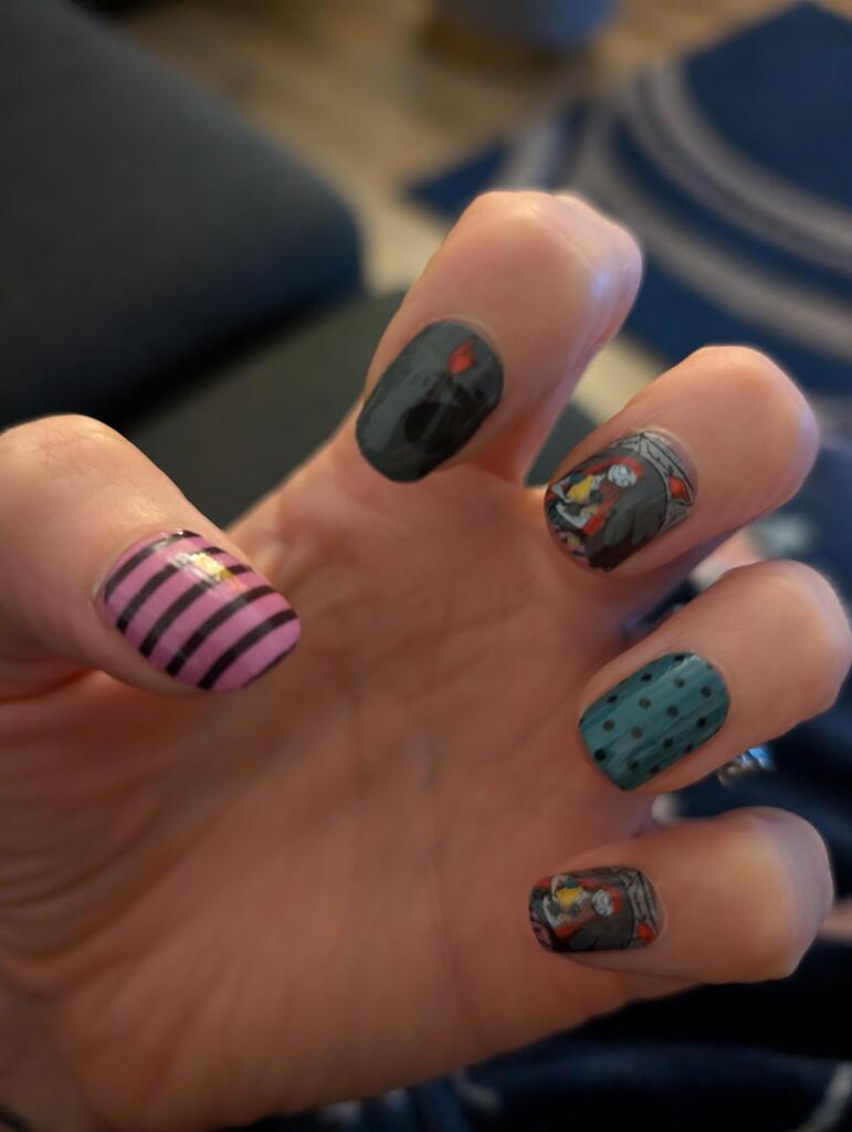 Hand displaying Halloween nail art with black stripes, polka dots and spooky character designs on nail wraps