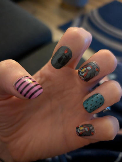 Hand displaying Halloween nail art with black stripes, polka dots and spooky character designs on nail wraps