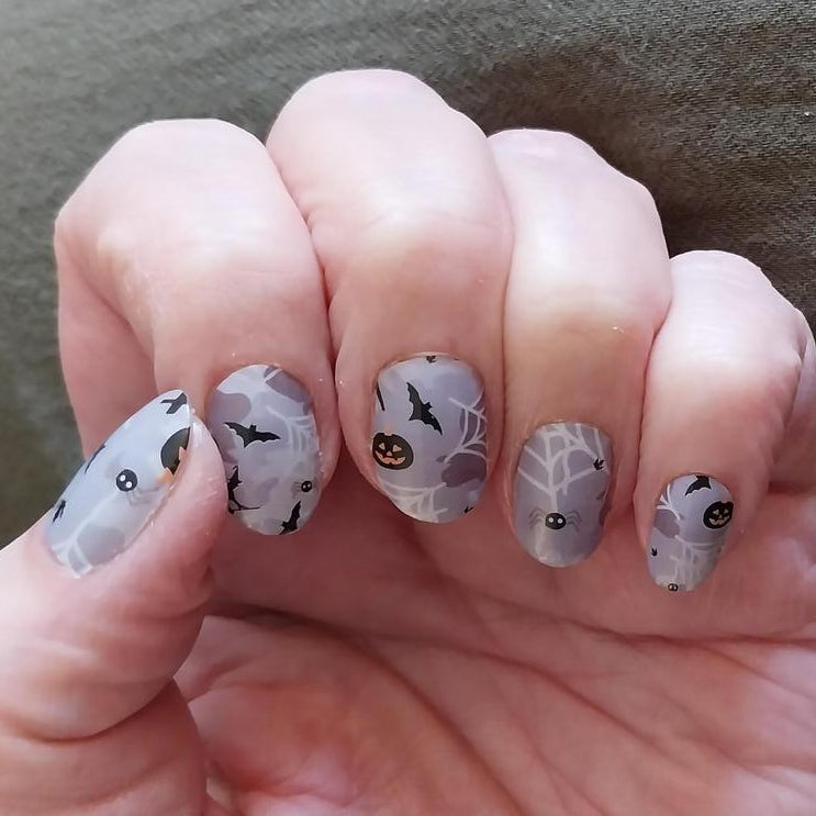 Halloween nail wraps on hand showing grey spooky design with pumpkins and spider web