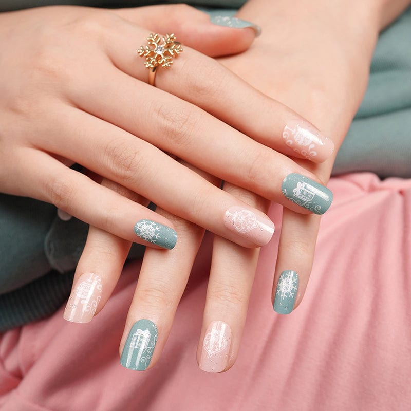 Hands wearing festive nail wraps in sage blue and dusty pink with Christmas snowflake designs