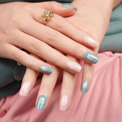 Hands wearing festive nail wraps in sage blue and dusty pink with Christmas snowflake designs