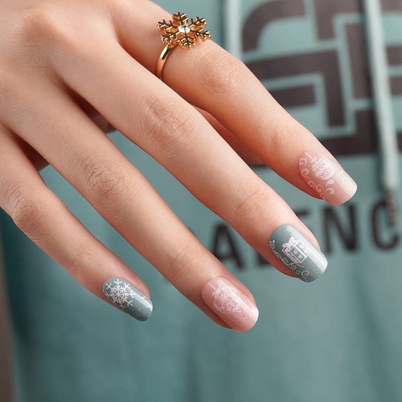 Hand showing festive nail wraps in muted sage and dusty pink with winter snowflake patterns