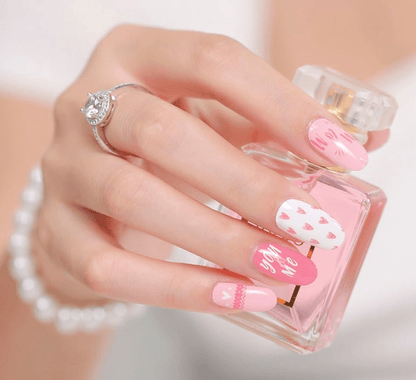 Hand holding perfume bottle wearing pink heart nail wraps with romantic designs