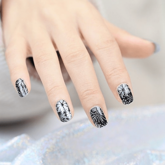 Black and silver firework starburst pattern nail wraps on hand showing dramatic metallic nail art