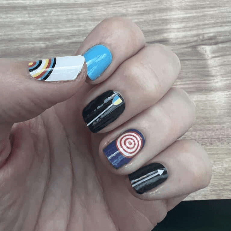 Non-UV nail wraps on hand featuring blue, black, white geometric target patterns for archery-inspired nail art
