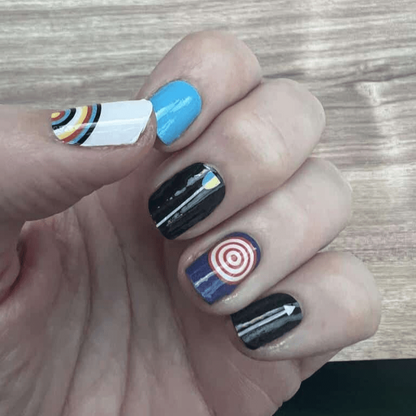 Non-UV nail wraps on hand featuring blue, black, white geometric target patterns for archery-inspired nail art