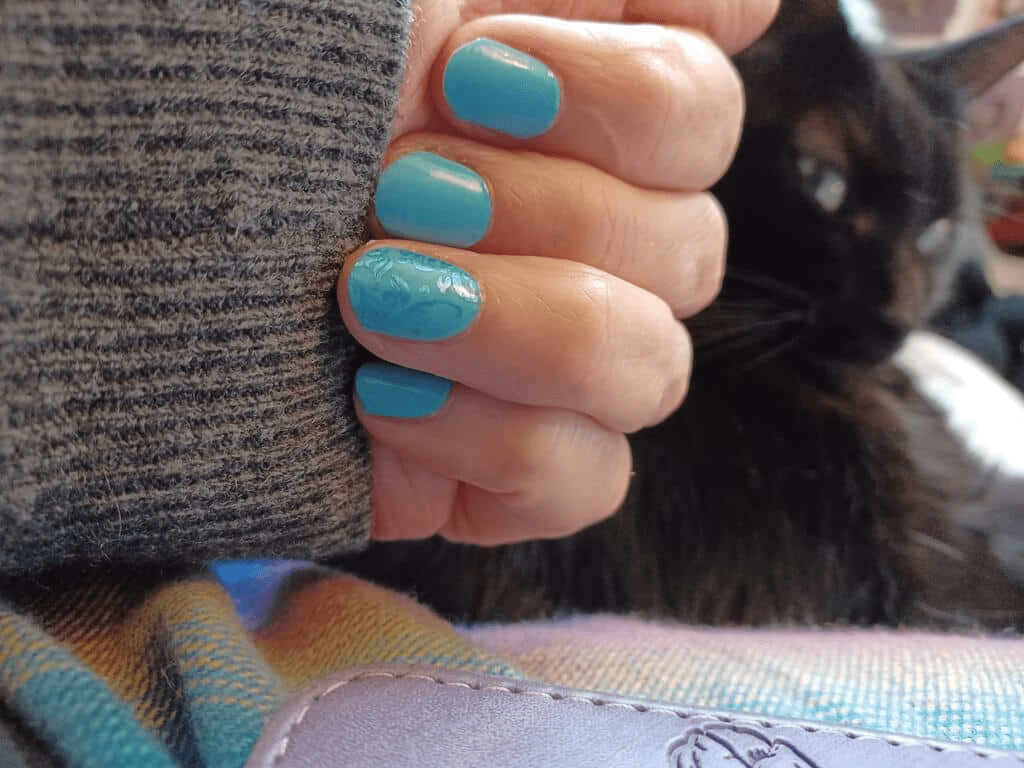 Hand wearing turquoise blue glossy nail wraps showing ocean-inspired at-home manicure