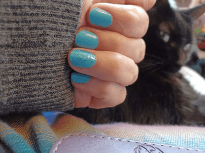 Hand wearing turquoise blue glossy nail wraps showing ocean-inspired at-home manicure