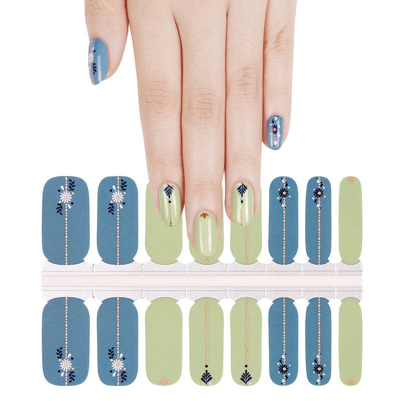 Hand wearing blue and sage green nail wraps with folk art daisy and leaf patterns