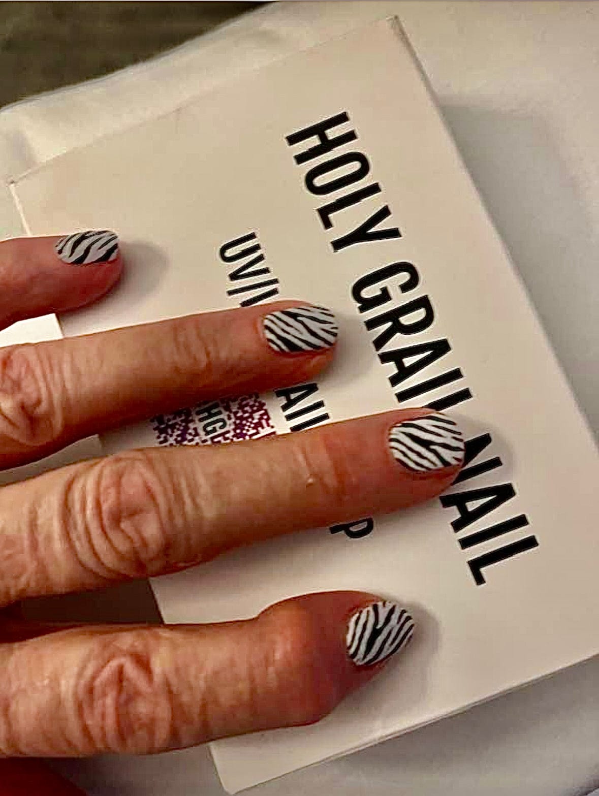 Hand wearing zebra print nail wraps with black and white stripes on packaging background