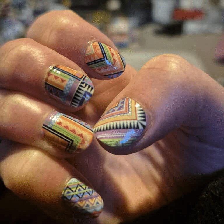 Hand displaying vibrant multicolour geometric nail art with rainbow chevron and stripe patterns using nail wraps