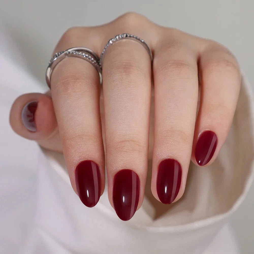 Deep burgundy red glossy short almond press-on nails on hand with rings