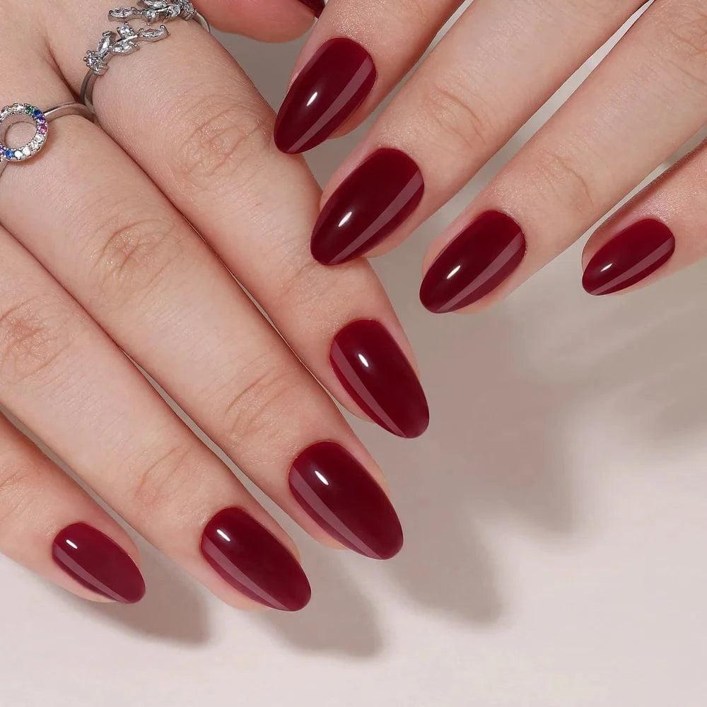 Deep burgundy glossy press-on nails short almond shape on hand with silver rings
