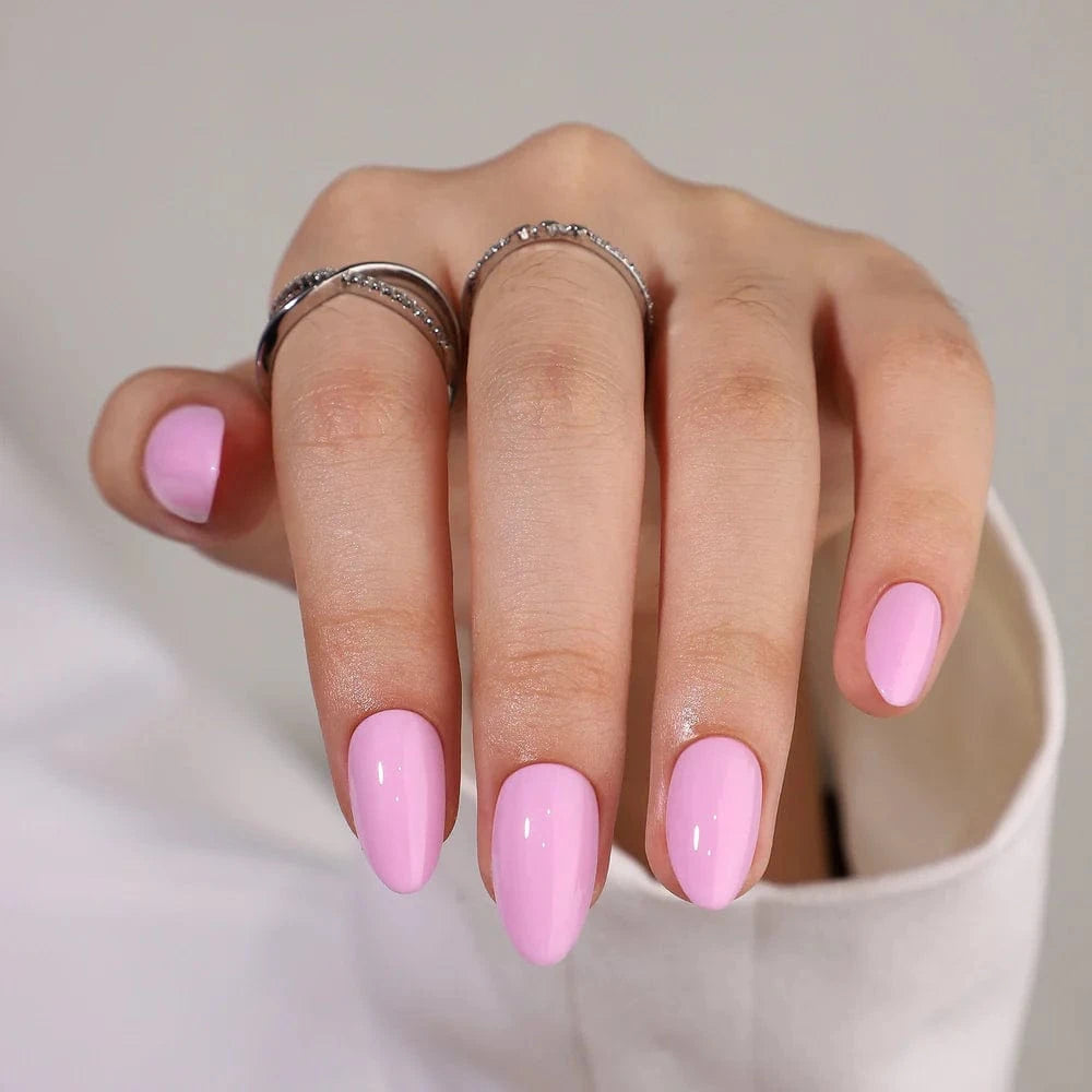 Pink glossy press-on nails in short almond shape on hand with silver rings