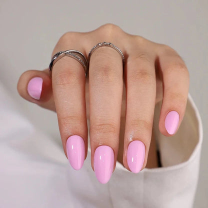 Pink glossy press-on nails in short almond shape on hand with silver rings