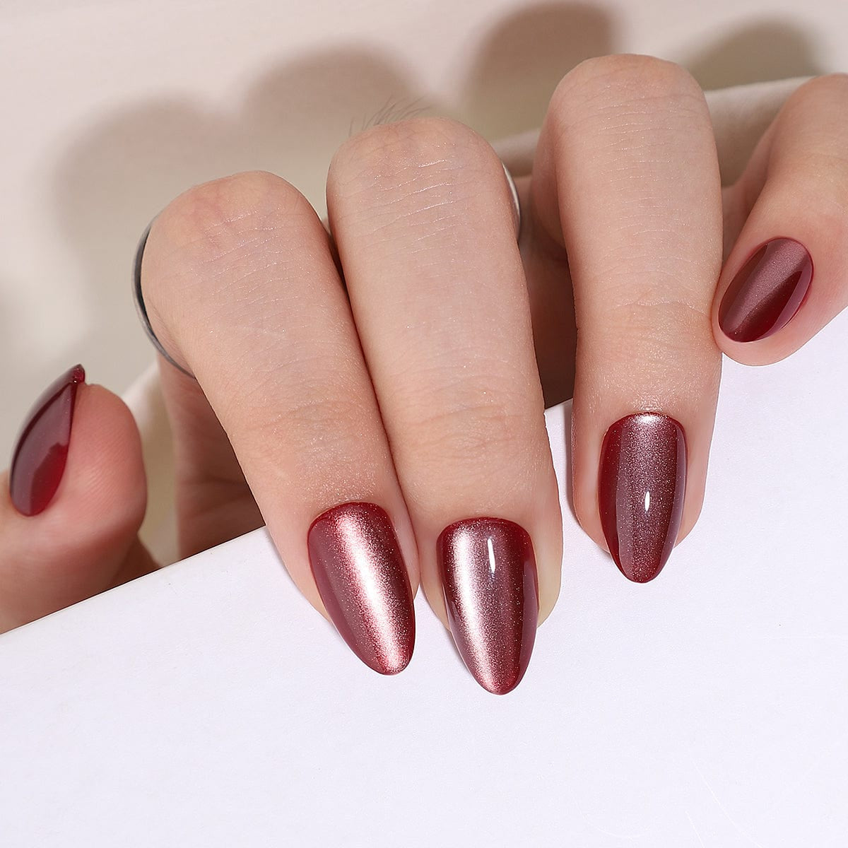 Deep burgundy cat's eye press-on nails with magnetic shimmer effect on hand