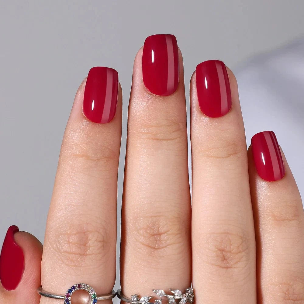 Glossy deep red press-on nails in short square shape on hand with silver rings