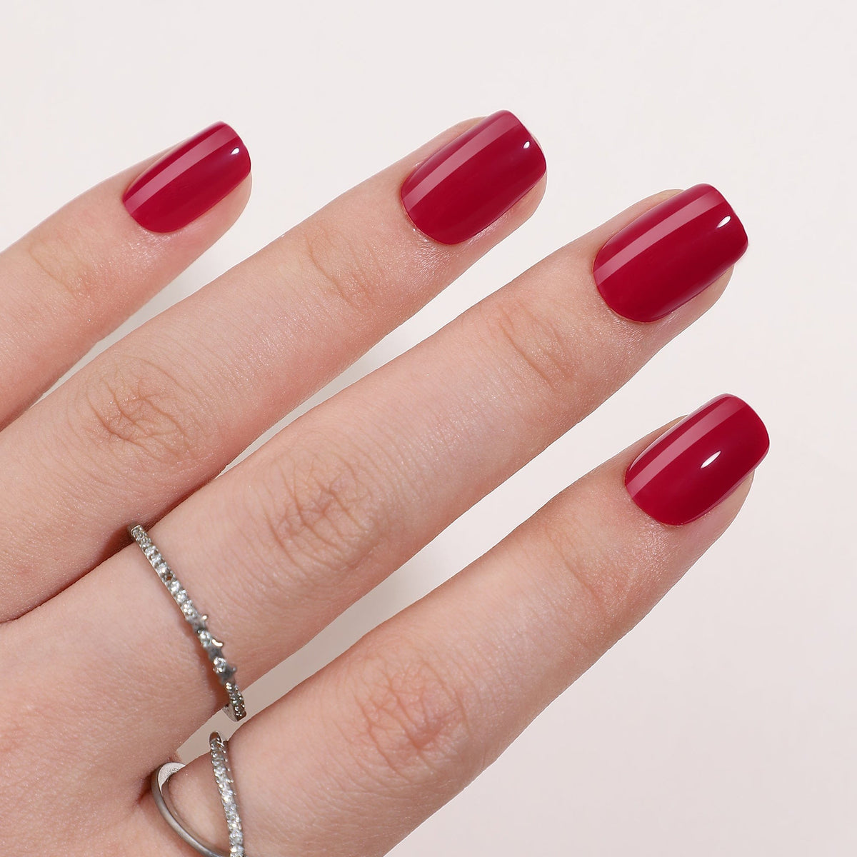 Glossy red short square press-on nails displayed on hand with rings