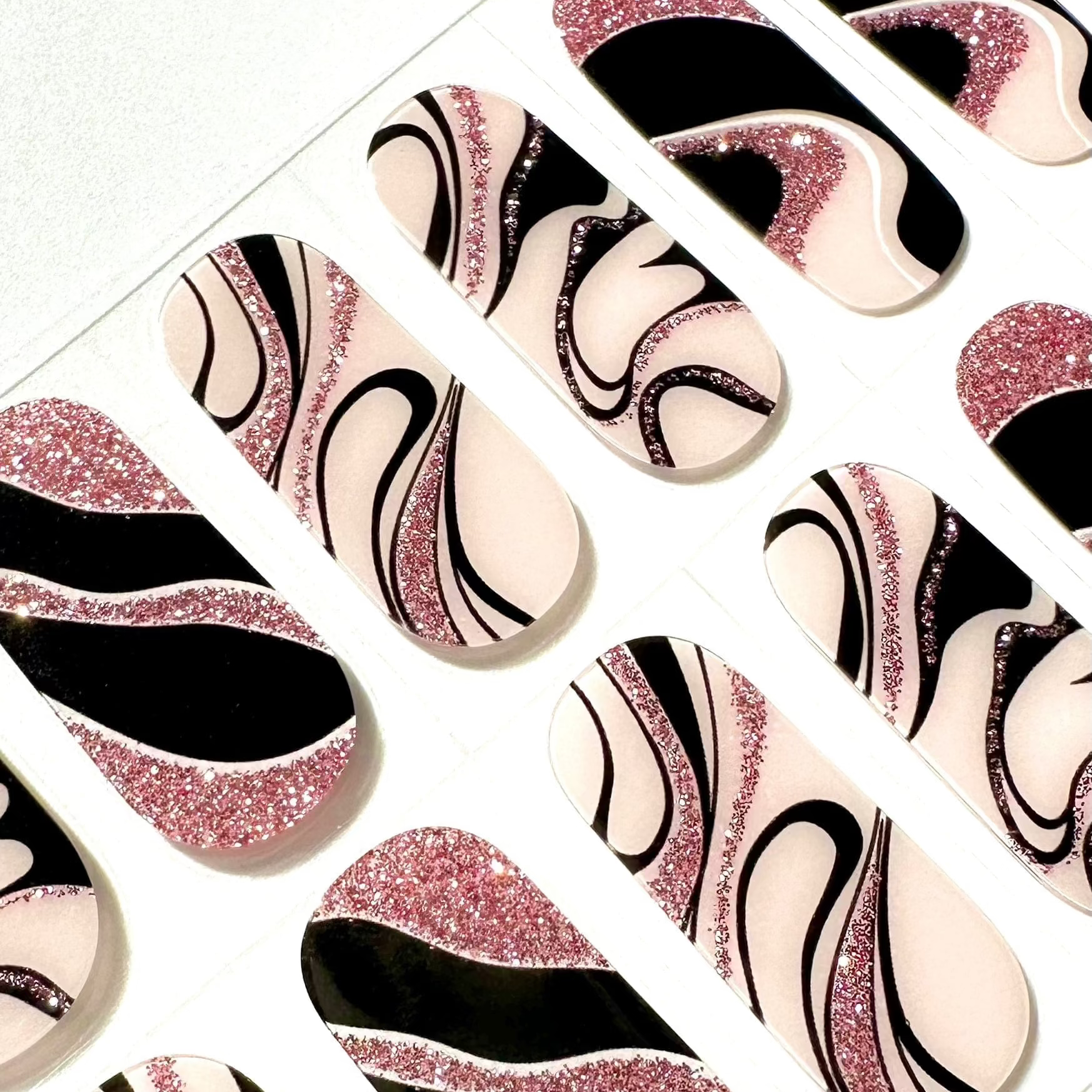 Close-up of pink glitter black marble gel nail wraps with artistic swirl patterns